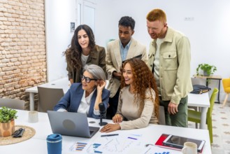 Diverse business team working together in a modern office, grouping around a laptop and microphone,