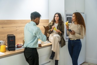Diverse colleagues chatting and smiling during a casual office kitchen break, two women holding