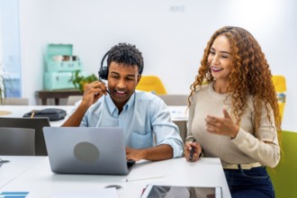 Diverse colleagues at an office desk collaborate as a man with a headset uses a laptop while a