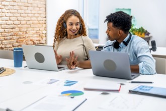 Diverse male and female coworkers with headsets collaborate at laptops on a bright modern office