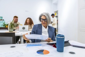 Mature female manager reviewing a financial report with charts and graphs on a table, collaborating