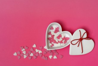 Sugar hearts in a heart-shaped bowl on a pink background