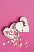 Sugar hearts in a heart-shaped bowl on a pink background