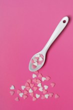 Sugar hearts with spoon on pink background