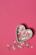 Sugar hearts in a heart-shaped bowl on a pink background