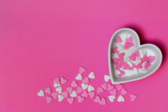Sugar hearts in a heart-shaped bowl on a pink background