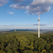 View of the television tower above a green forest under a blue sky with soft clouds,