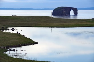 Calm sea inlet with rocky arch in the background and cloudy sky, Horsehead, Eshaness, Shetland