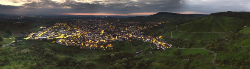 Hilly landscape with illuminated town at sunset under a cloud cover, Korb im Remstal,