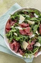 Fresh arugula salad with prosciutto and grated parmesan cheese, on a plate, homemade, no people
