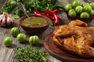 Baked tobacco chicken, served with tkemali sauce, on a wooden table, Georgian cuisine, rustic