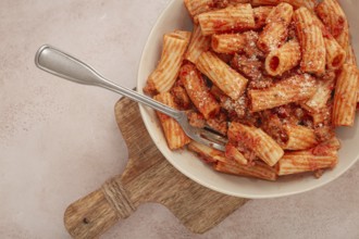 Rigatoni pasta with meat sauce and parmesan cheese on a light table, top view, homemade, no people