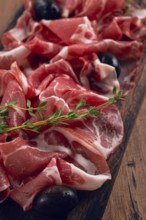 Freshly cut dried meat, served with olives and herbs, on a wooden chopping board, no people