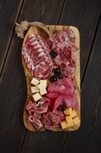 Assorted, sliced meat appetizer, prosciutto, salami and ham, with cheese and olives, on a wooden