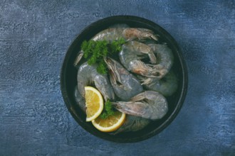 Fresh raw white-footed shrimp, tiger prawns vannamey, on a clay plate, with lemon and herbs, on a