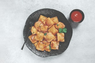 Fried ravioli with parmesan cheese, served with red sauce and garnished with herbs, on a black