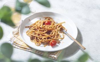 A plate of perfectly cooked spaghetti is topped with rich sauce and fresh tomatoes. Next to it, a