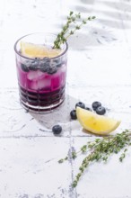 Refreshing blueberry and thyme drink served with lemon in a clear glass on a light surface