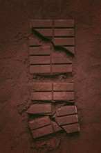 Chocolate bars broken and scattered on cocoa powder background with rich texture and color