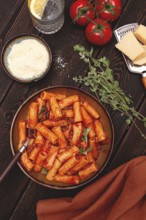 Rigatoni pasta with meat sauce and parmesan cheese on a dark wood table with ingredients, top view