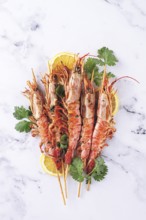 Shrimps on skewers, Grilled, spread on a marble surface, garnished with lemon slices and fresh