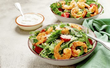 Two bowls of shrimp salad, arugula and cherry tomatoes, with parmesan cheese, healthy food