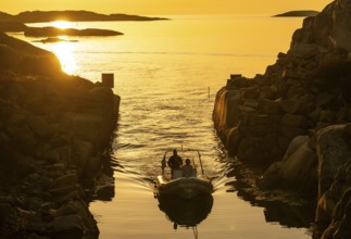 Motorboat with two persons sailing in harbour entrance at sunset, archipelago, Smögen,