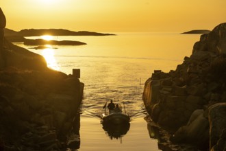 Motorboat with two persons sailing in harbour entrance at sunset, archipelago, Smögen,