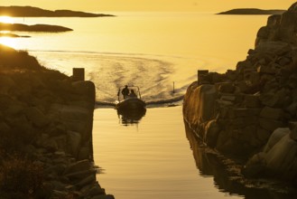 Motorboat with two persons sailing in harbour entrance at sunset, archipelago, Smögen,