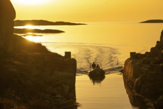 Motorboat with two persons sailing in harbour entrance at sunset, archipelago, Smögen,