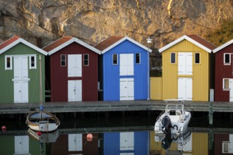 Colourful boathouses and boats in the calm water in front of rocks in the harbour of Smögen,