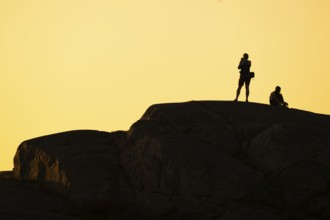 Silhouette of two tourists photographing the sunset on a rock, Smögen, Smögenbryggan, Västra