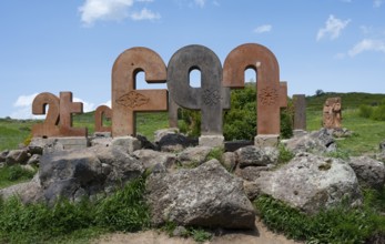 Stone pillars with traditional motifs, surrounded by large rocks and green grass, monument to the