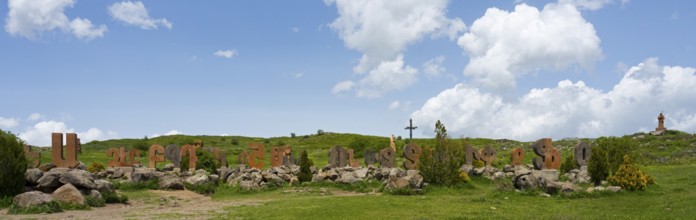 Wide landscape with rocks and a cross, surrounded by green meadow and blue sky, monument of the