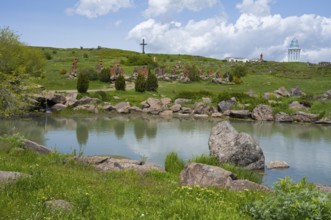 Peaceful lake surrounded by rocks and green landscape with a cross on a hill, monument of the