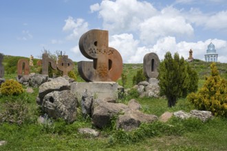 Stone sculptures in the shape of letters on a green meadow, surrounded by rocks and bushes under a