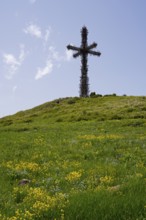 Large metal cross on a hill with a green meadow and yellow flowers under a blue sky, Monument to