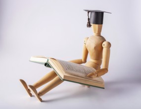 Wooden man in a student cap sits on the floor and reads a book, copy space