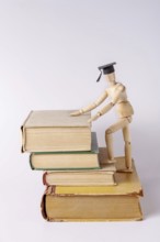 A wooden man in a student cap climbs up steps made from textbooks