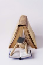 A wooden man in a student cap lies under an open book and reads a textbook, space for text