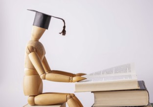 A wooden man in a student cap is reading a book