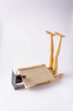 A wooden man in a student cap lies on the floor under an open book