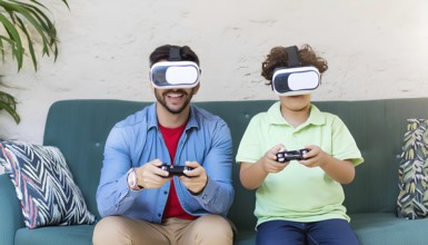 A man and a boy are playing a video game together on a couch. The boy is wearing a green shirt and