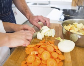 A cozy kitchen scene showing only hands of a couple preparing food, chopping vegetables, and