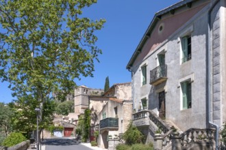 The sunlit village street of Moureze is lined with traditional stone houses with reddish-brown