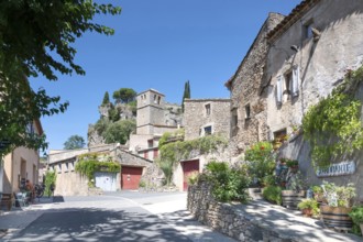 The sunlit village street of Moureze is lined with traditional stone houses with reddish-brown