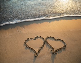 Warm tropical beach with two hearts drawn on the sand, blue waters, and clear skies, invoking