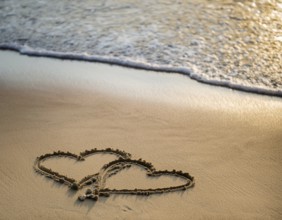 Warm tropical beach with two hearts drawn on the sand, blue waters, and clear skies, invoking