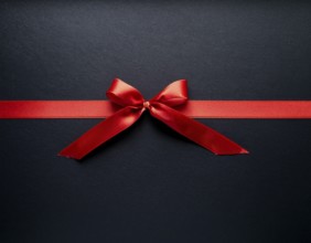 A beautifully wrapped gift box adorned with red satin ribbons forming a bow, contrasting against a