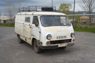 An old white van parked on the side of the road in a rural area, rust decoration visible, van,
